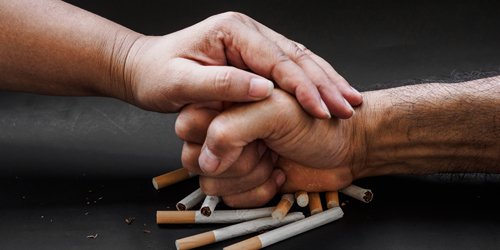 Man hand and woman hand punching and destroy cigarettes on black background. Quitting smoking concept.